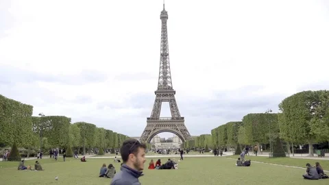 Man walking past Eiffel Tower people on grass Champ de Mars Paris France Stock Footage 94001679