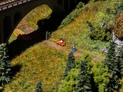 A man is walking on a path in a field with a toy train set Stock Photos