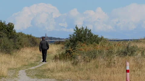 Man walking on a path toward a distant lighthouse Stock Footage 343854205