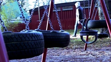 Man walking by a playground, with a swing Stock Footage 85490730