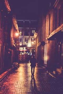 Man walking in rainy lit alley Stock Photos