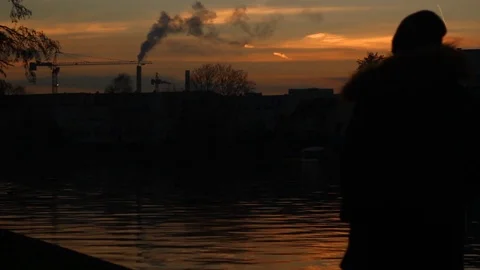 Man walking by a river at sunset with a factory in the background Video stock 100242856