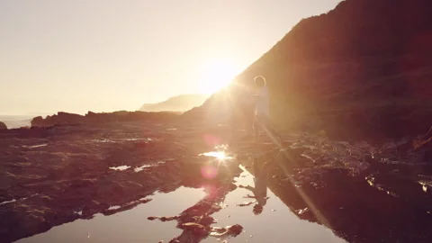 Man walking on the rocks by the ocean as the sun is setting Stock Footage 279797816
