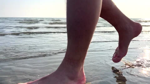 Man walking on a sandy beach with coastal city in the background. Slo mo CU Stock Footage 234698583