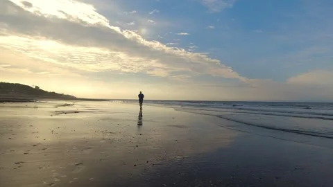 Man walking on sandy beach at sunset with cloudy sky and birds. 4K Stock Footage 308419432