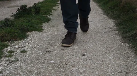 Man walking on sandy road towards the camera, stops on the road, grass on sides Stock Footage 43181665