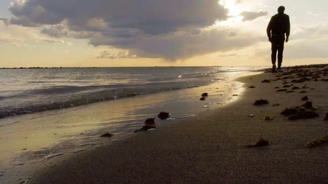 Man walking on the sea beach, beautiful sunset, seaside with a sand. Cloudy sky Stock Footage 80388248