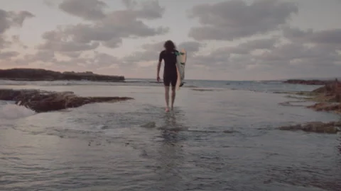 Man walking in shallow water by the beach with his surfboard Stock Footage 275160895
