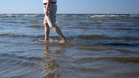 Man walking on shallow water from right to left by the sea on the sand beach 스톡 동영상 89994284
