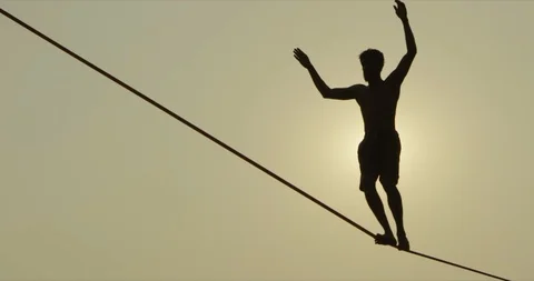 Man walking on a slack line / high line / tight rope. He is silhouetted by the Video stock 93415796