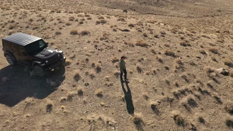 A man walking slowly out in front of his Jeep parked off-road on a hill top l Stock Footage 169975396