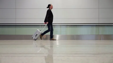 Man walking with small carry-on suitcase in airport terminal Stock Footage 320118770
