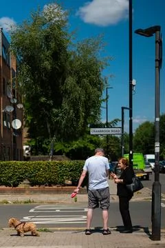 Man walking a small dog while chatting with an elderly woman on a sunny Lon.. Stock Photos
