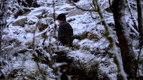 Man walking up the snowy mountain with trees in foreground Stock Footage 233514061