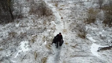 Man walking on snowy path carrying items in winter landscape with buildings in b Stock Footage 329431518