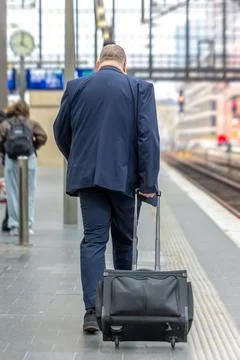 Man walking with suitcase on train platform. Rail travel and commute content. Stock Photos