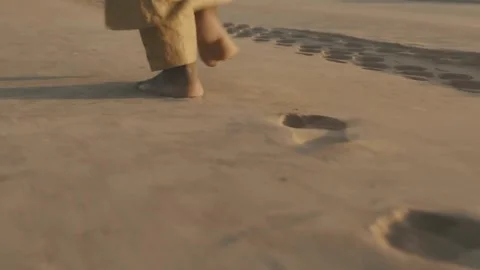 Man Walking on Sunset Sand in Flowing Robe and Yellow Pants Stock Footage 321379099