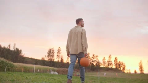 Man walking through field holding pumpkin at sunset 库存影片 219405394