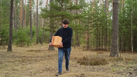 Man walking through a forest carrying a cut log in his hands. 库存影片 334441283