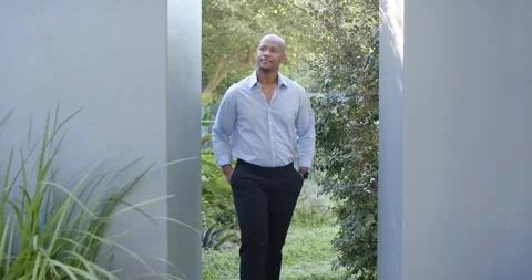 Man walking through garden passage in blue shirt, adjusting wristwatch, leaning Stock Footage 339592099
