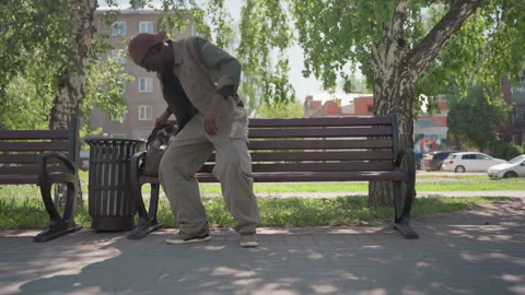 Man Walking Through Park Carrying Backpack Approaching Benches Under Trees With Stock Footage 345839022