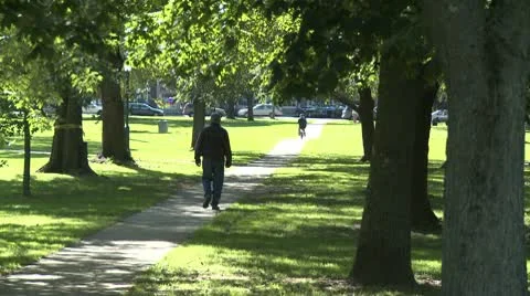 Man walking through park with a person on a bike ahead of him Stock Footage 10684424