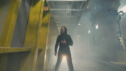 Man walking through a smoke filled industrial corridor in dramatic light Vidéo 339492540
