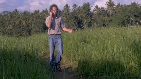 Man walking through tall grass on a path talking on a cell phone Video stock 90818498
