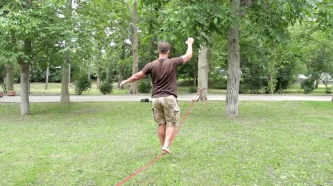 Man walking on a tightrope in the park, from the back Stock Footage 53780294