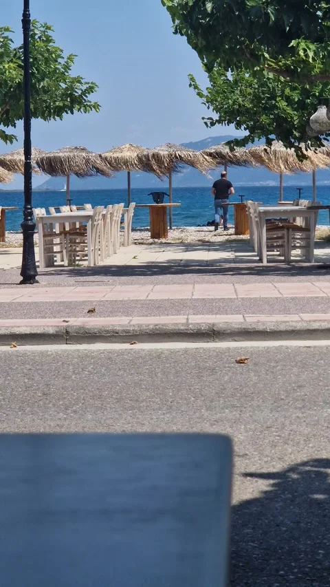 Man Walking Toward Beachside Taverna with Straw Umbrellas – 4K Summer Scene Stock Footage 317942253