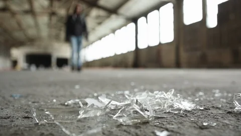 Man walking toward broken bottle glass on the floor of a warehouse Stock Footage 88052121