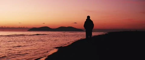 A man walking toward the camera on the beach at sunset Stock Footage 324461914