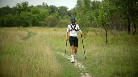 Man walking toward camera with trekking poles on grassy nature trail Stock Footage 313951283