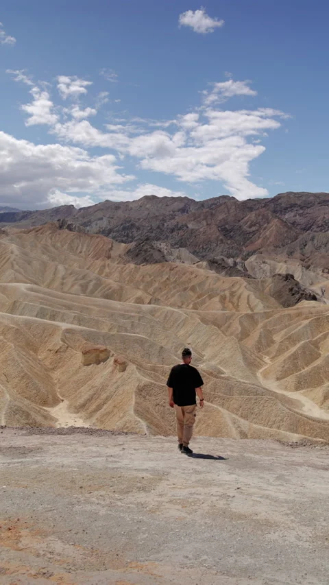 Man Walking Toward Eroded Desert Badlands Under Blue Sky with White Clouds. Stock-Footage 342937534