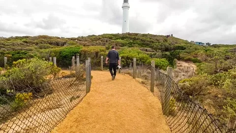 Man Walking Toward Lighthouse on Scenic Path Vídeos de archivo 306838731