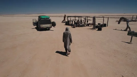 Man Walking Toward Vehicle and Structures in African Desert Stock Footage 301368643