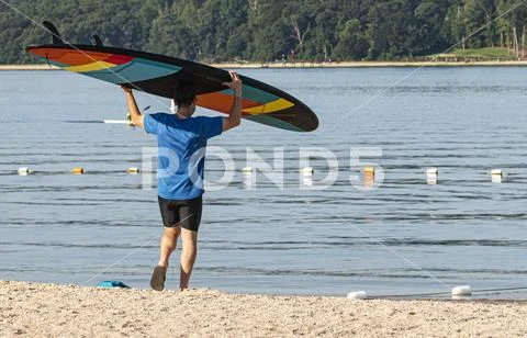 Man walking toward water with paddle board on his head Stock Photos