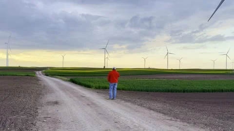 Man Walking Toward Wind Turbines Across Rural Fields at Sunset Video stock 335215615