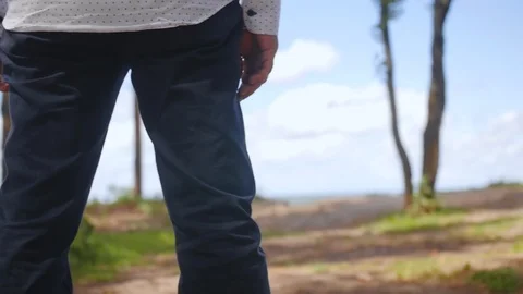 Man walking towards edge of a cliff, looking over the sea. Medium shot. Stock Footage 113274973