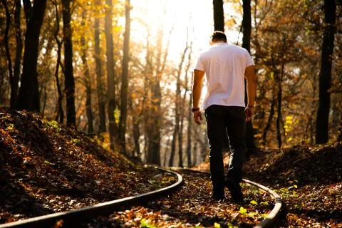 Man walking on train rails on fall with leaves on the ground during sunset Stock Photos