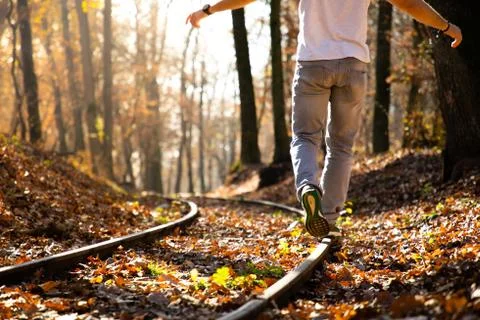Man walking on train rails on fall with leaves on the ground during sunset Stock Photos