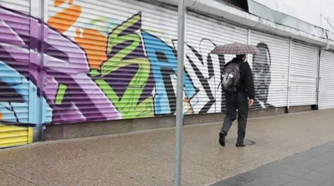 Man walking with umbrella in front of graffiti Stock Footage 44183092