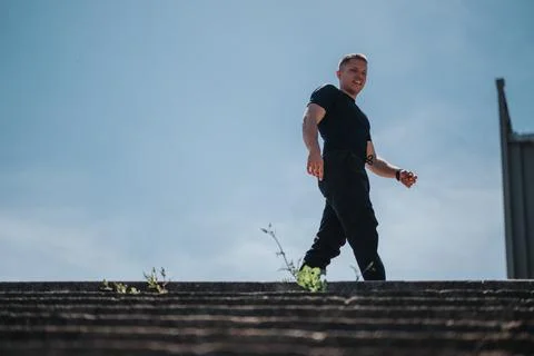 Man walking under clear sky with urban background and green elements Foto stock