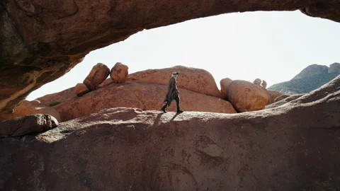 Man Walking Under Rock Arch in African Desert Stock Footage 301368826