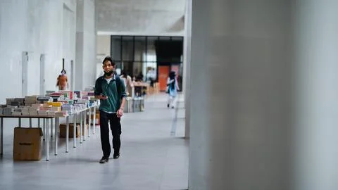 A man is walking while holding a cellphone in his right hand at an exhibition Stock Photos