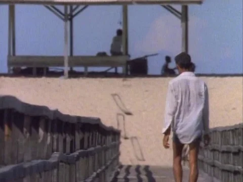 Man walking on a wooden deck towards the sandy beach on a sunny day Video stock 79926041