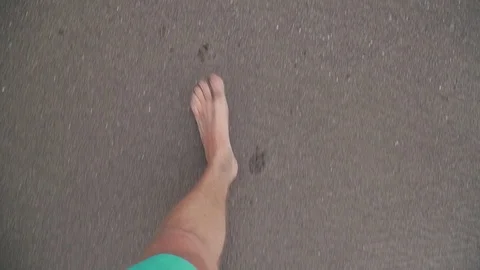 A man walks along the beach in the frame only legs top view sand and waves 库存影片 126976332