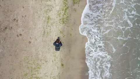 A man walks along an empty sea beach controlling a drone top view Video stock 157705970