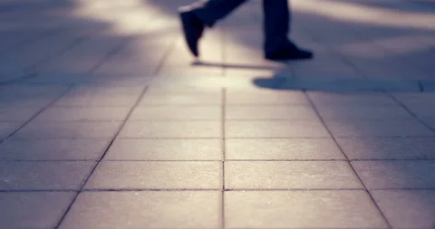 A man walks along the pavement with paving slabs and casts a shadow in the sun  Stock Footage 119614927