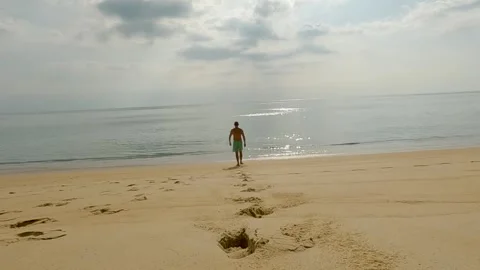 A man walks along a sandy beach into the sea, rear view Stock Footage 307135442